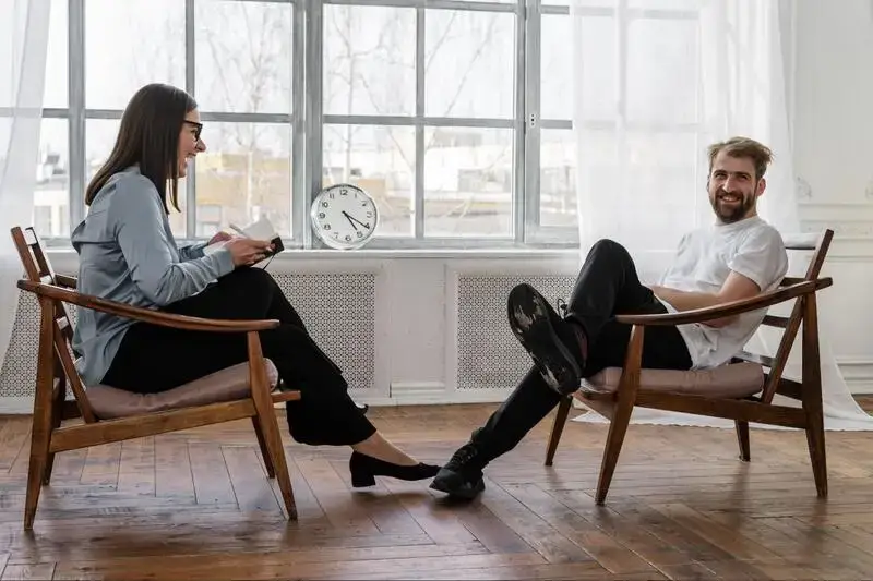 a woman therapist and a man sitting on the chairs, talking and laughing