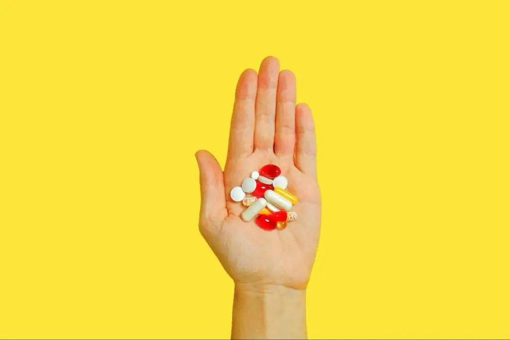 A stretched out hand holding a mix of different pills and capsules