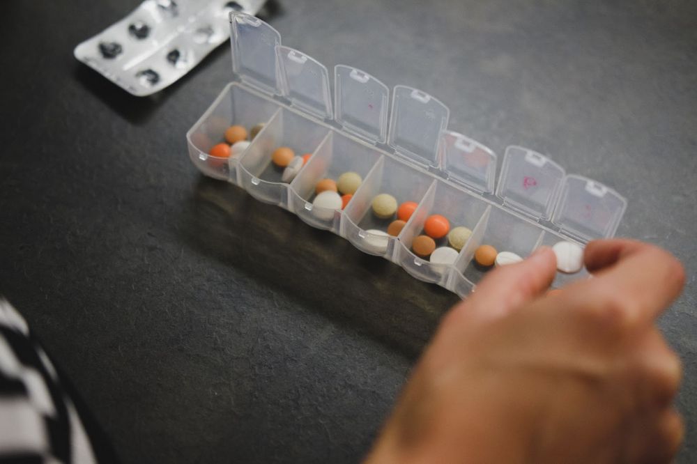 A person putting a pill into a plastic pill box