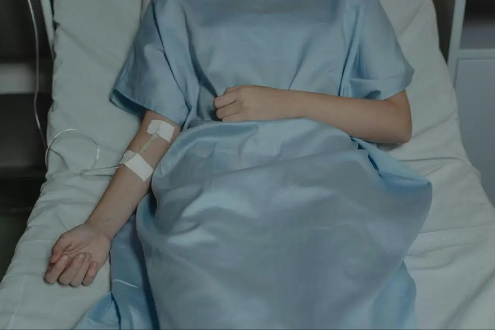 A patient rests in bed dressed in a hospital gown, connected to an IV drip